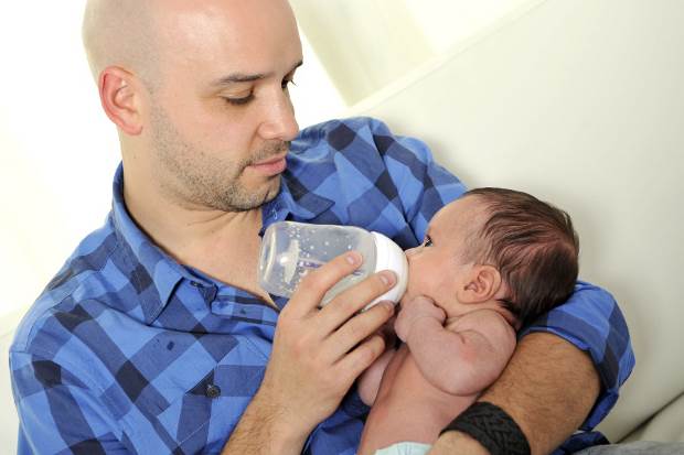 young father feeding newborn baby with milk bottle on couch at home